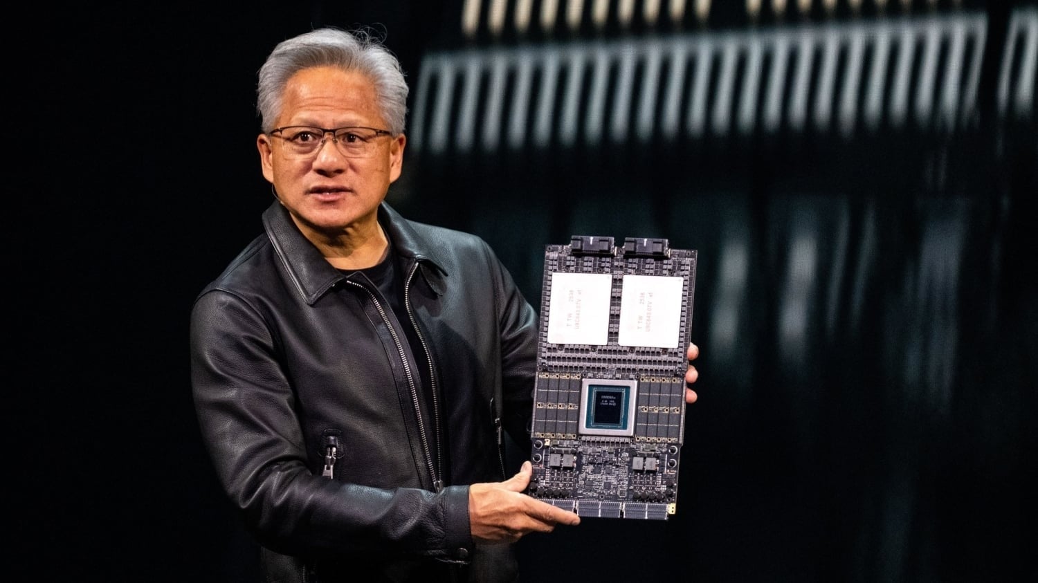 Jensen on stage with a GPU board: the hardware is the visible half of a business now pitching a recurring software line. (Image: TweakTown, Oct 25, 2026)